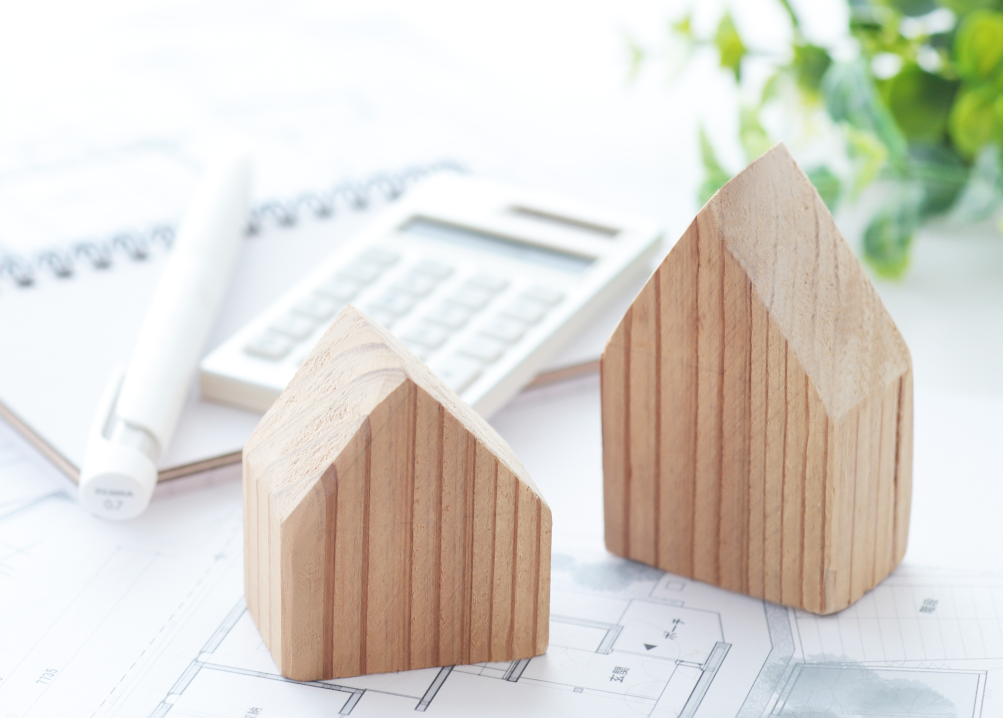 家の形をした木が2つと電卓とペンとノートがある