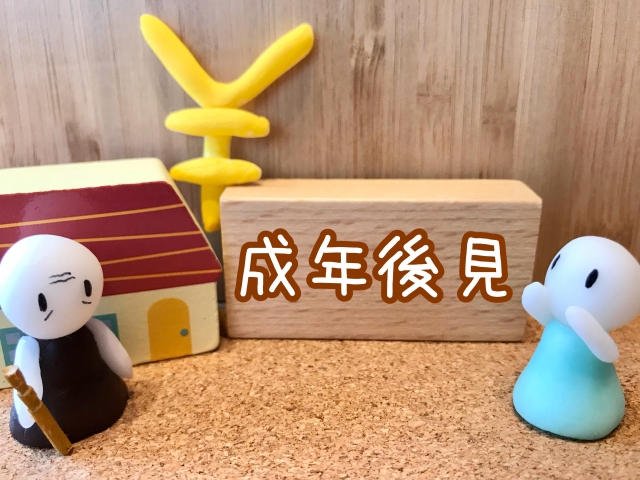 成年後見という文字が書かれた木の手前に杖をもった人形と両手をあげている人形がある