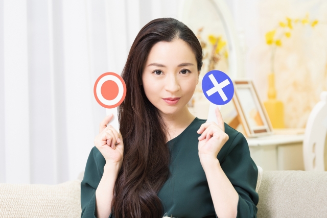 緑色の服を着た女性が右手にマルのプラカード、左手にバツのプラカードをもっている