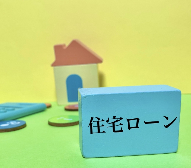 住宅ローンという文字が書かれた水色に塗られた木の後ろに家の模型がある