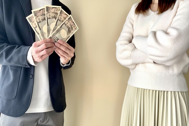 腕組みした女性とジャケットを着た男性がお札を手で広げて持っている