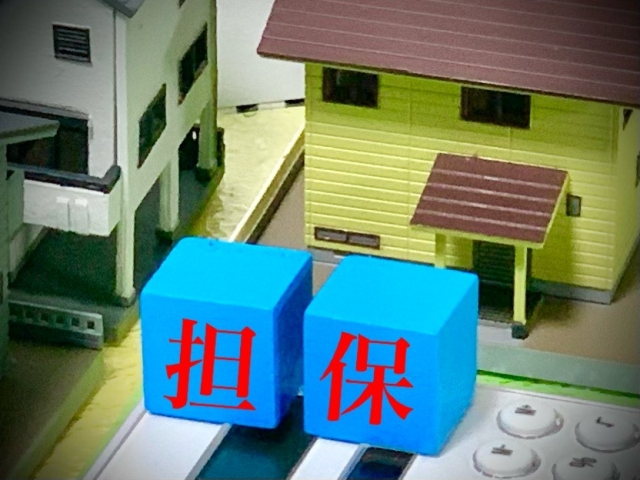 家の模型の前に積み木で担保という字が書いている